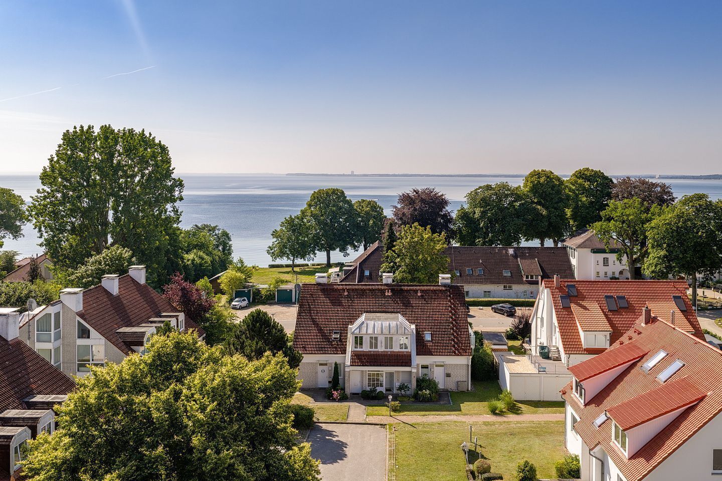 Un quartier résidentiel avec des maisons, un ciel dégagé et une étendue d’eau en arrière-plan.