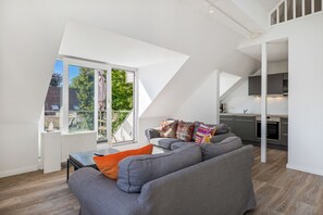 Ein modernes Wohnzimmer mit grauem Sofa, einem Esstisch und einer Küchenzeile.