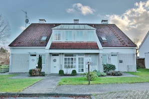 A two-story house with a red-tiled roof, white exterior, and a front entrance with a door and windows.