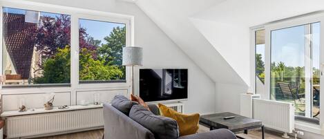 Ein modernes Wohnzimmer mit großem Fenster, Flachbildfernseher und einer Couch.