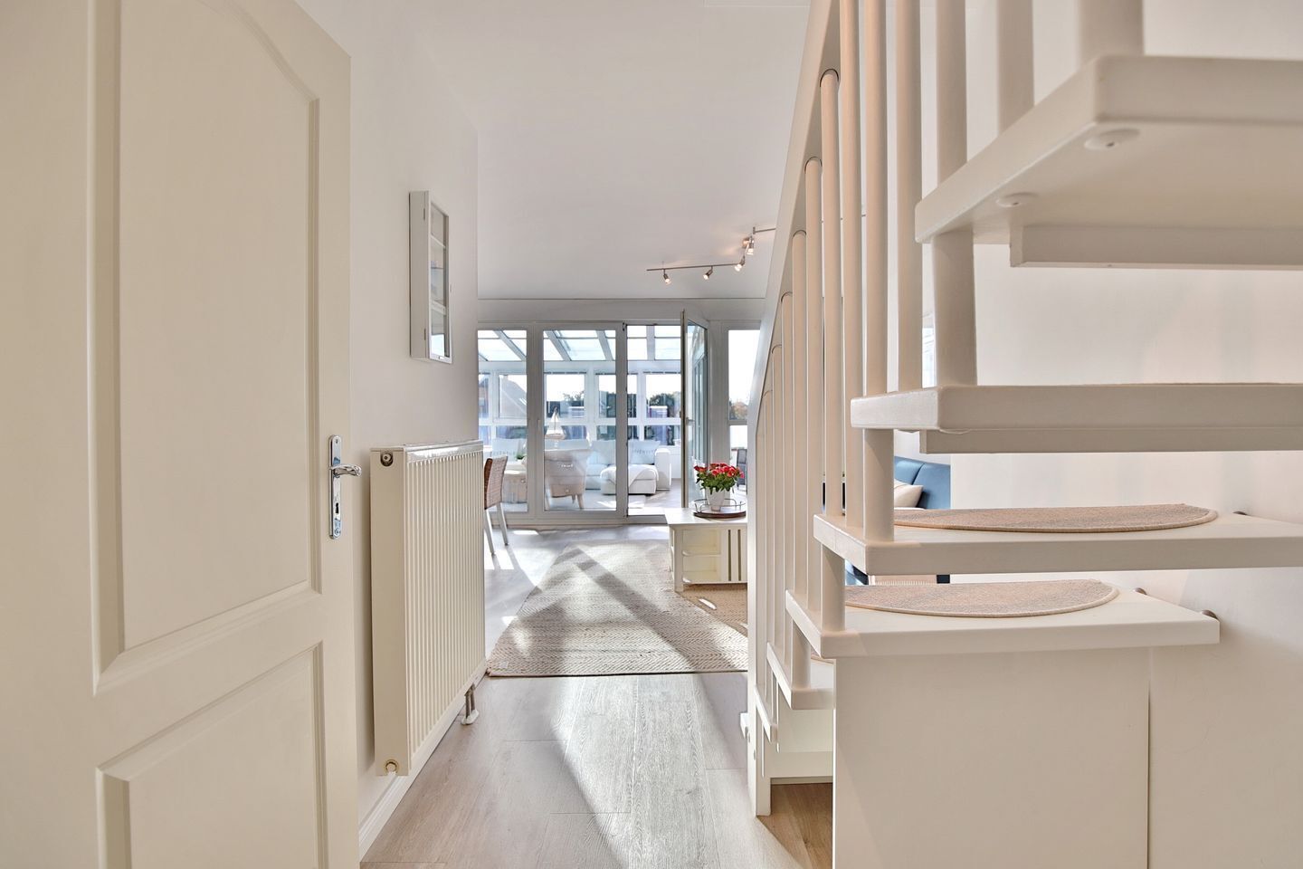A modern interior with a central hallway leading to a bright room with large windows.