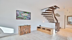 A modern interior with a spiral staircase, a wooden console table, and a large abstract painting. - Haus Oberdeck, Deutschland (Scharbeutz)