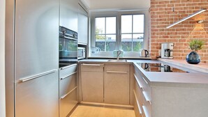 A modern kitchen with stainless steel appliances, a brick wall, and a large window. - Haus Oberdeck, Deutschland (Scharbeutz)