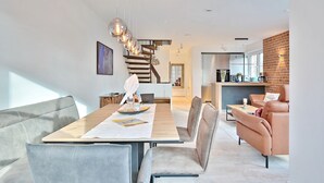 A modern dining area with a wooden table, grey upholstered chairs, and pendant lighting. - Haus Oberdeck, Deutschland (Scharbeutz)