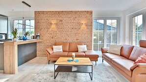 A modern living room with a brick wall, two sofas, a coffee table, and a kitchen area with a countertop and appliances. - Haus Oberdeck, Deutschland (Scharbeutz)