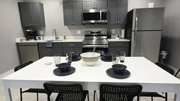 Une cuisine moderne avec des meubles gris, un réfrigérateur en acier inoxydable et une table à manger blanche, agrémentée d’assiettes et de bols noirs.