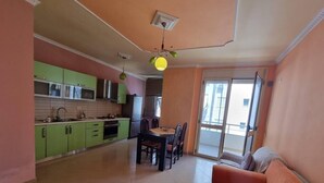 A spacious living area with a dining table and chairs, a kitchen with green cabinets, and a large window providing natural light.