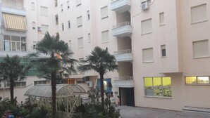 A multi-story building with balconies, a covered outdoor area with plants, and a large window with a view.