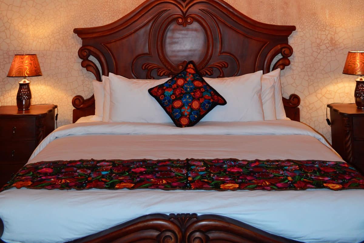 A bedroom with a wooden ceiling, a chandelier, a bed with a floral bedspread, and two bedside lamps.