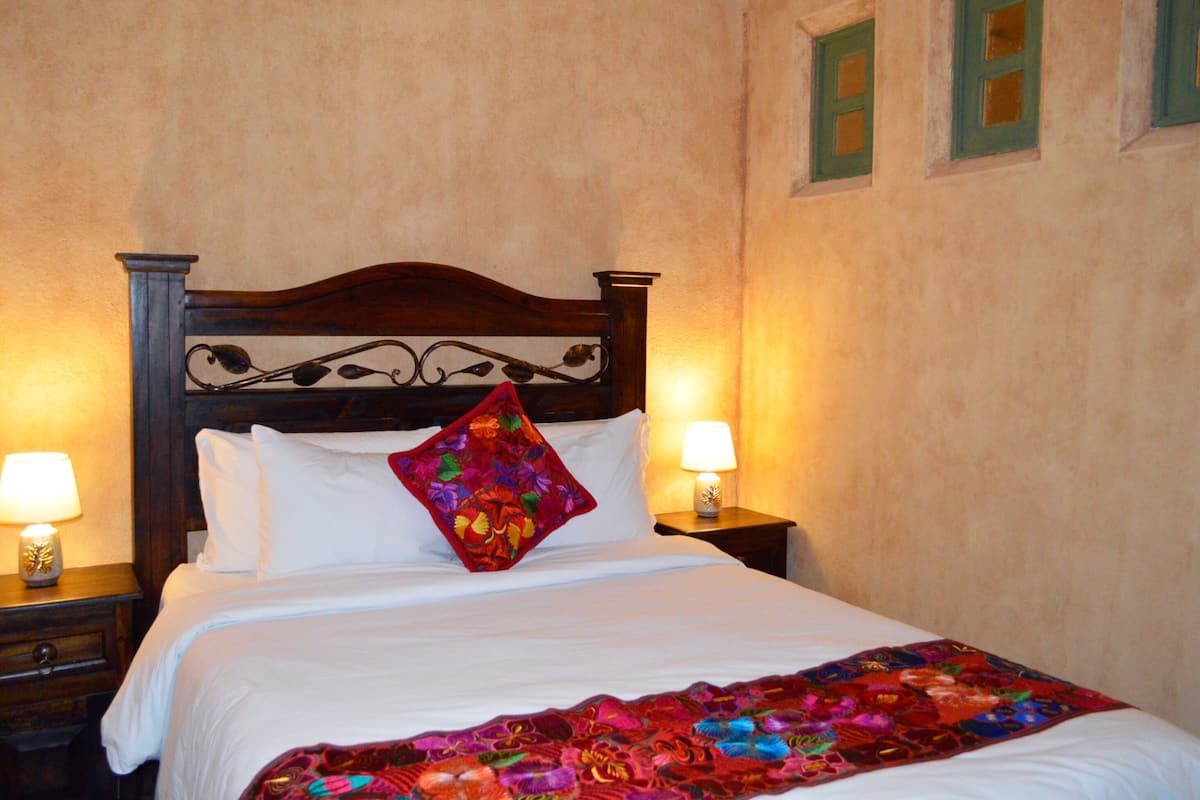 A bed with a wooden headboard, white bedding, a colorful throw blanket, and two bedside lamps.