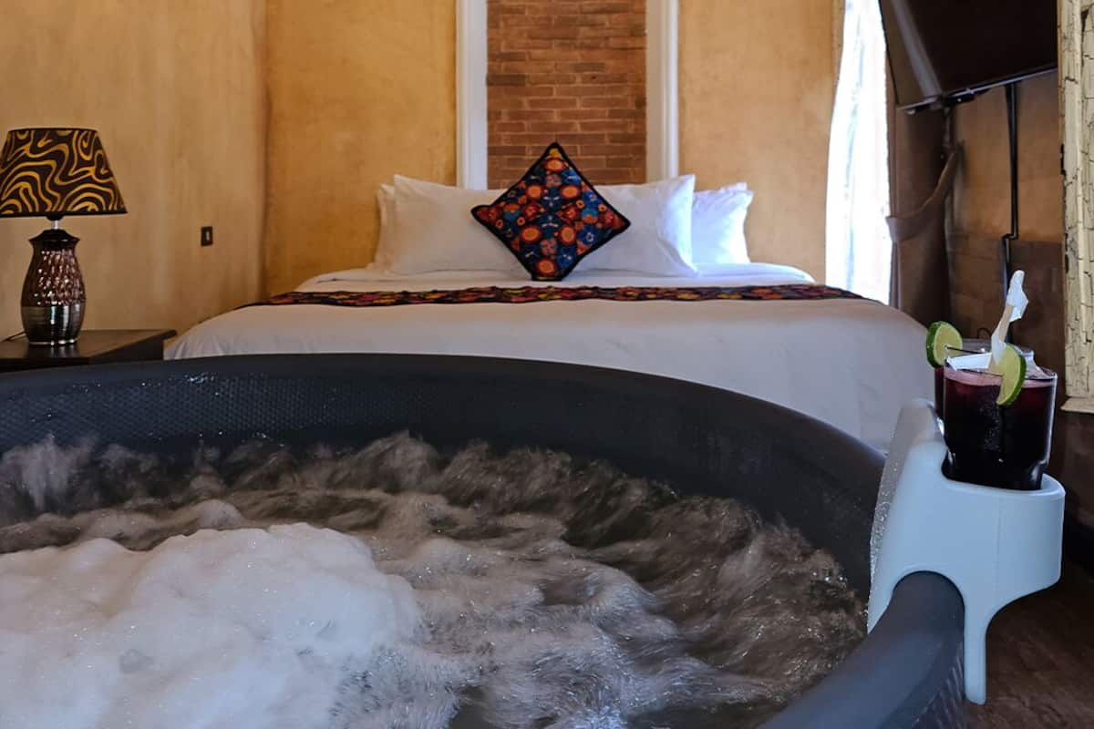 A room with a bed, a TV, a lamp, and a hot tub.