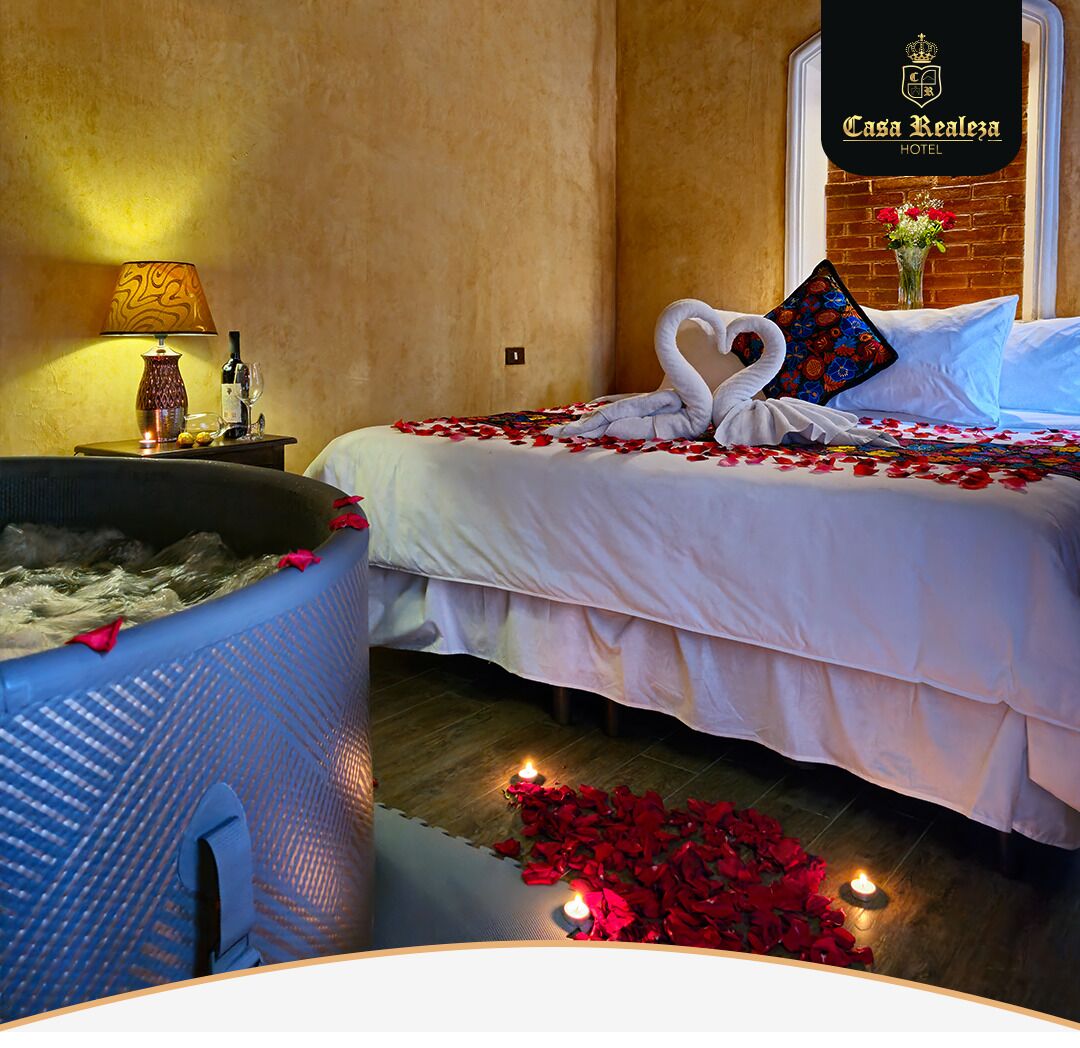 A hotel room with a bathtub, a bed with rose petals and a heart-shaped towel, and a sign for Casa Realiza Hotel.