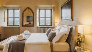 Ein Schlafzimmer mit Bett, zwei Fenstern, einem Heizkörper, einem Spiegel und einem Bild an der Wand.