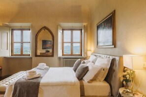 A bedroom with a bed, two windows, a radiator, a mirror, and a painting on the wall. - Apartments Florence - Villa La Medicea - swimming pool-Updated 2024 (Mezzomonte)