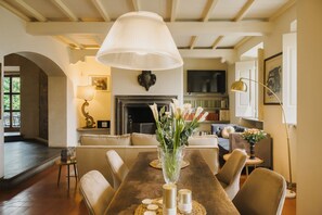 Un comedor con una mesa de madera, sillas, un jarrón con flores, una chimenea y un televisor al fondo.