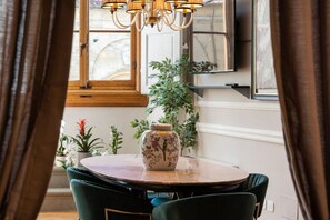 Un coin repas avec une table ronde, des chaises vertes, un vase orné de motifs floraux et un lustre.