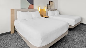 Quarto de hotel com duas camas, uma cabeceira de madeira, uma mesinha de cabeceira com telefone e luminárias fixadas na parede.