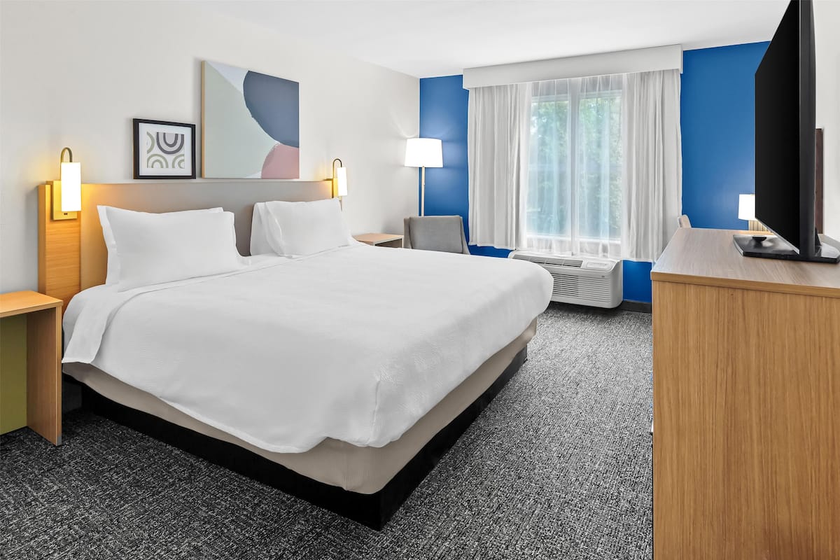 Ein Hotelzimmer mit einem großen Bett, Nachttischen, einem Schreibtisch, einem Fernseher und einem Fenster mit Vorhängen.