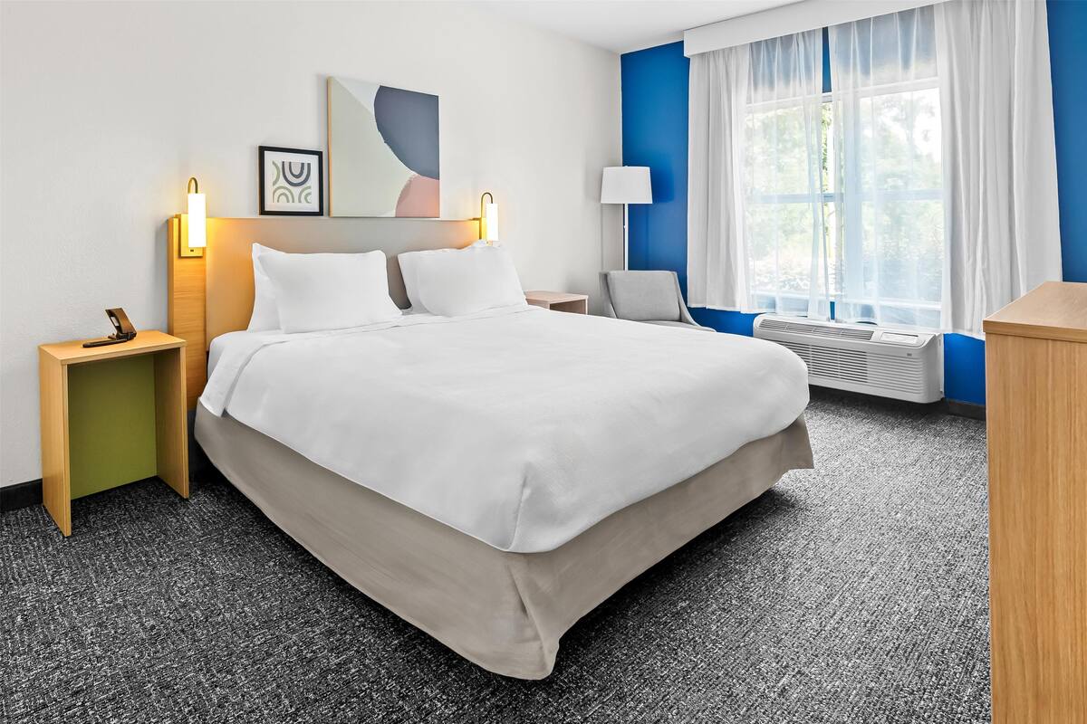 Ein Hotelzimmer mit einem großen Bett, Nachttischen, einem Schreibtisch und einem Fenster mit Vorhängen.