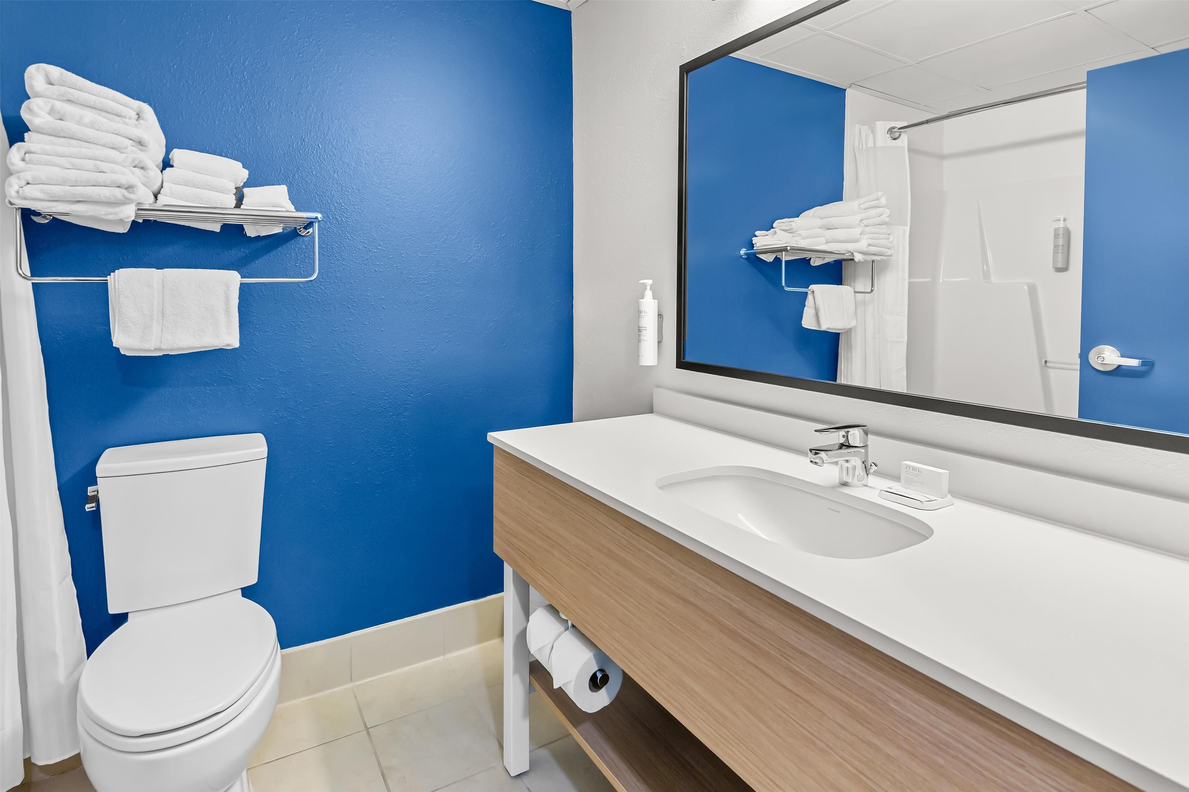 Un baño con pared azul, inodoro blanco y un lavabo con espejo arriba.