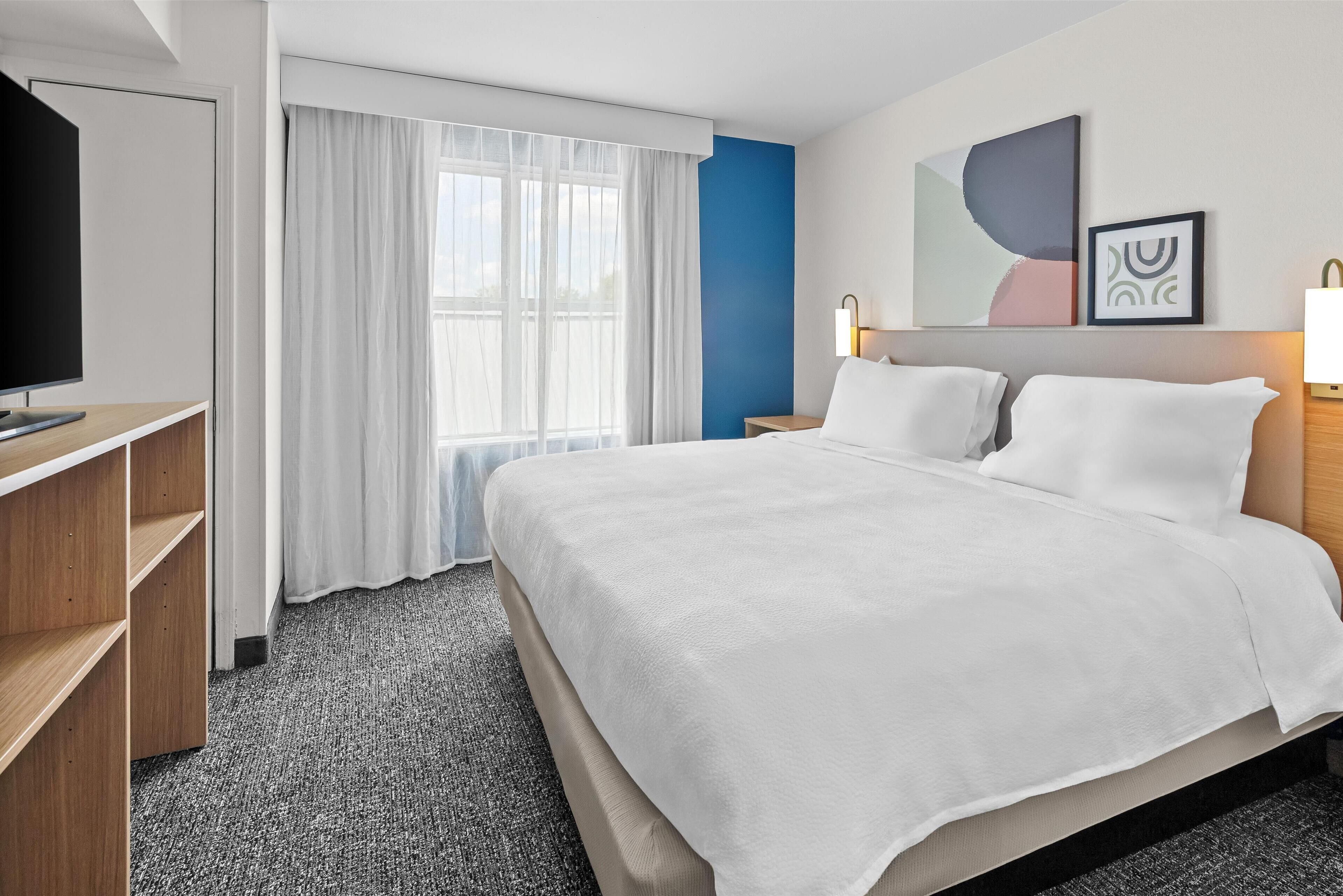 A hotel room with a bed, a TV, a desk, and a window with curtains.