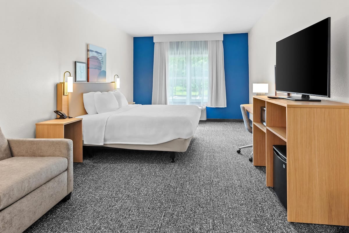 Ein Hotelzimmer mit Bett, Schreibtisch, Fernseher, Sessel und einem kleinen Mülleimer.