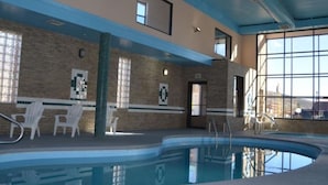 Una piscina interior con paredes de vidrio transparente, un muro de ladrillo y techo azul.