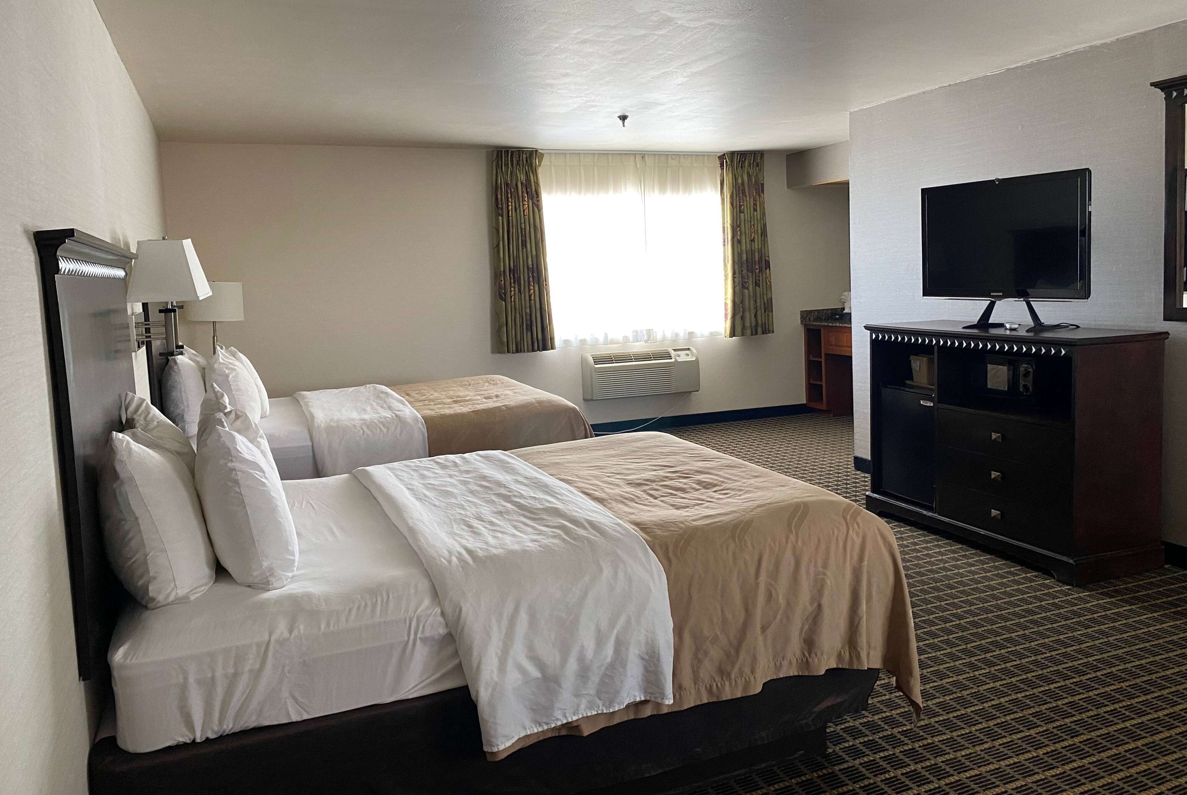A hotel room with two beds, a TV, a desk, and a window with curtains.
