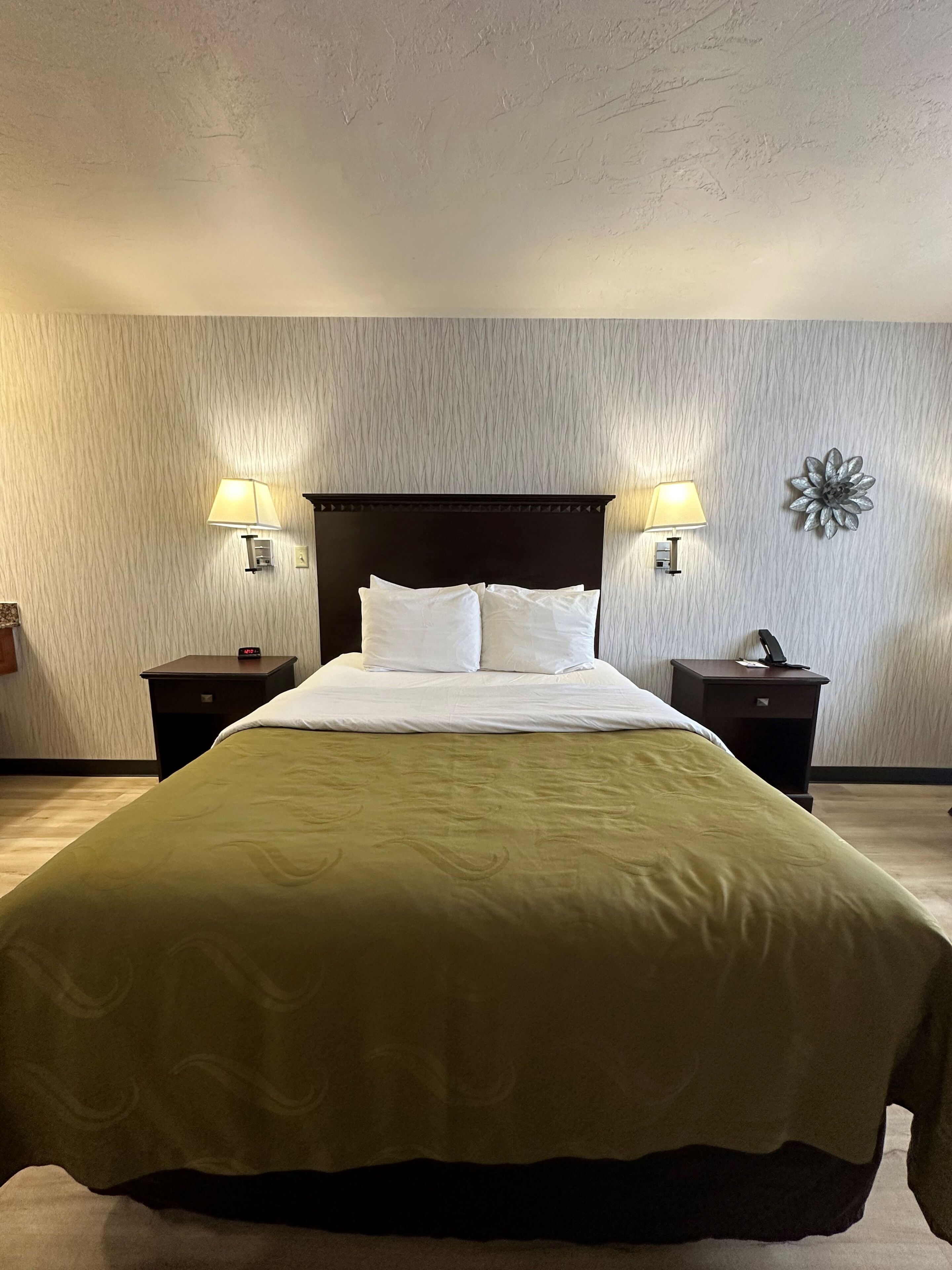 A hotel room with a large bed, two bedside tables with lamps, a decorative wall piece, and a textured wall.