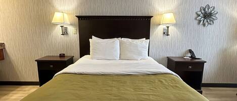 A hotel room with a large bed, two bedside tables with lamps, a decorative wall piece, and a textured wall.