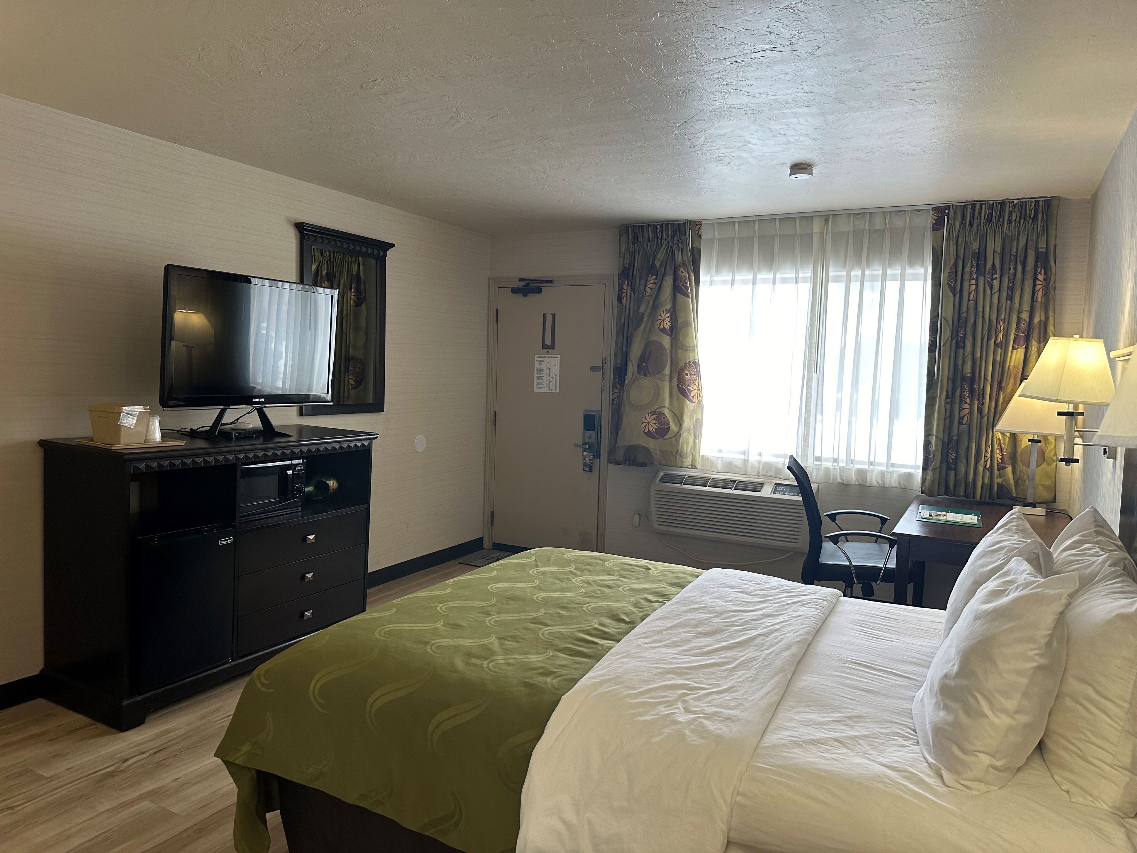 A hotel room with a bed, a desk, a television, a wardrobe, and an air conditioning unit.