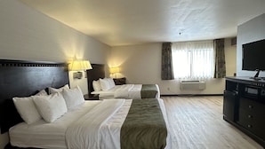 Una habitación de hotel con dos camas, televisión, escritorio y ventana con cortinas.