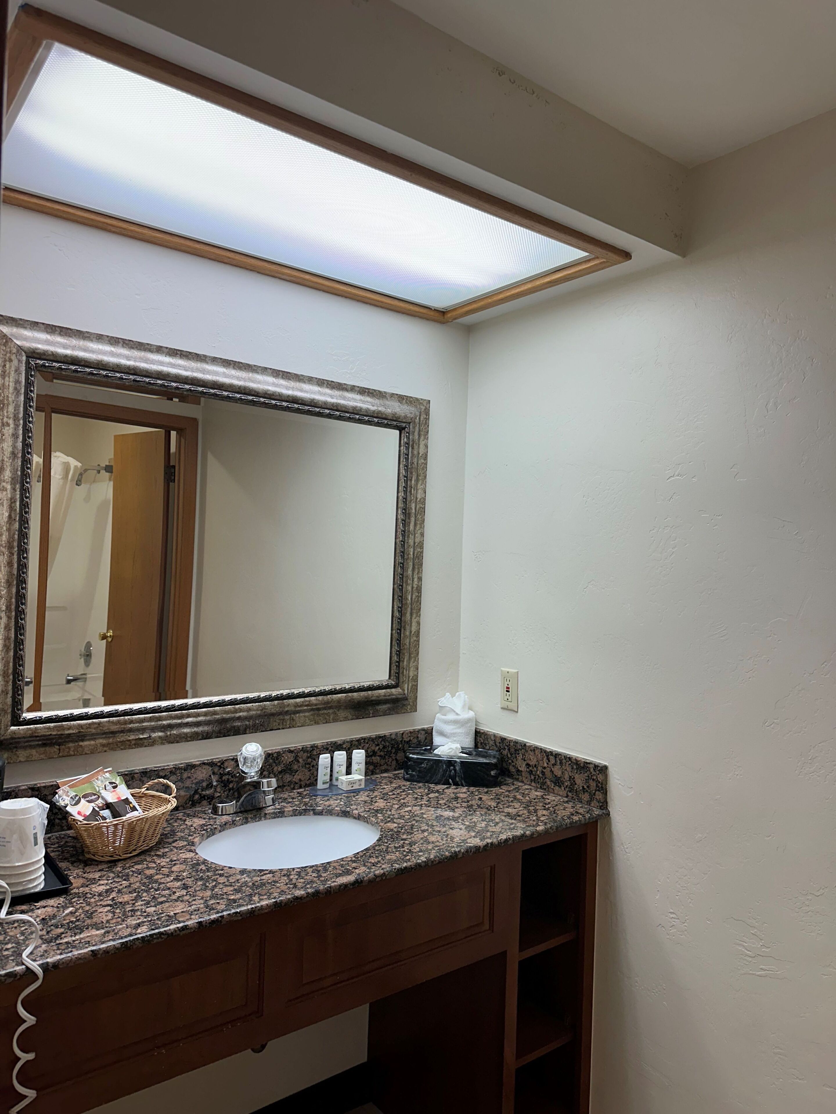 A bathroom with a granite countertop, a white sink, a large mirror, and a towel dispenser.