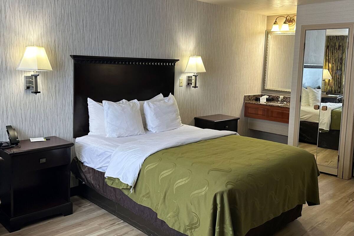 Habitación de hotel con una cama grande, dos lámparas de noche, una mesita de noche, un espejo y piso de madera.