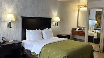 Quarto de hotel com uma cama grande, duas luminárias de cabeceira, mesa de cabeceira, espelho e piso de madeira.