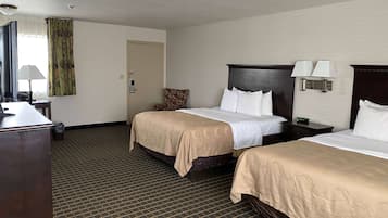 Une chambre d’hôtel avec deux lits, un bureau, une chaise, une lampe et une porte.