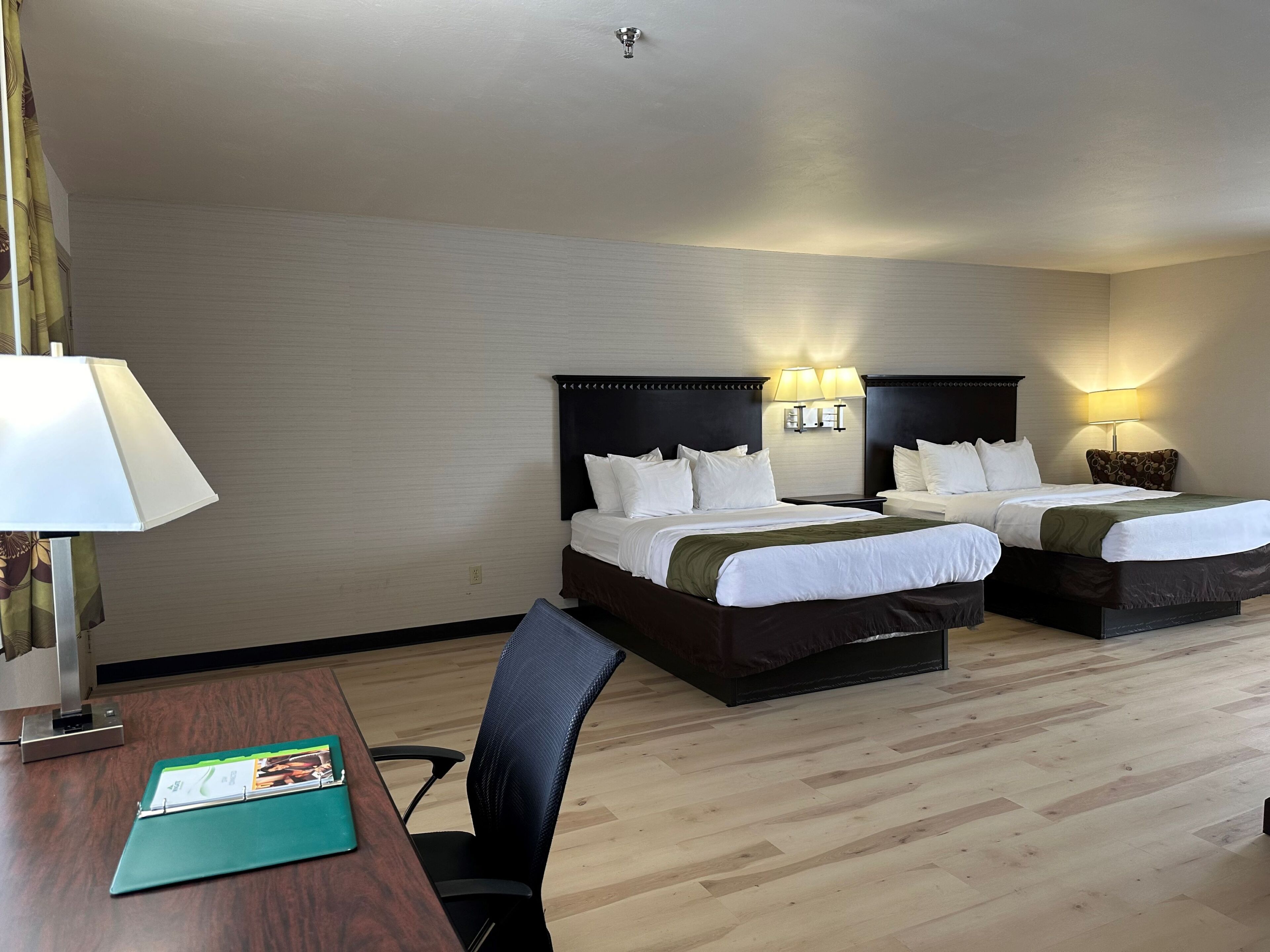 Una habitación de hotel con dos camas, un escritorio con lámpara y una silla.