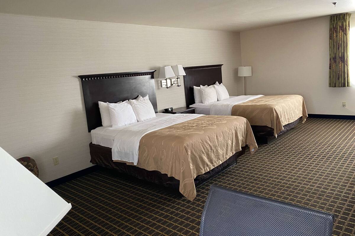 Habitación de hotel con dos camas, piso alfombrado y ventana con cortinas.