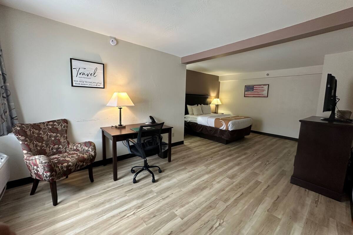 Habitación de hotel con cama, escritorio, silla y una mesita pequeña con una computadora.