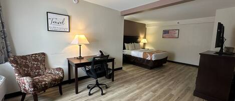 A hotel room with a bed, desk, chair, and a small desk with a computer.