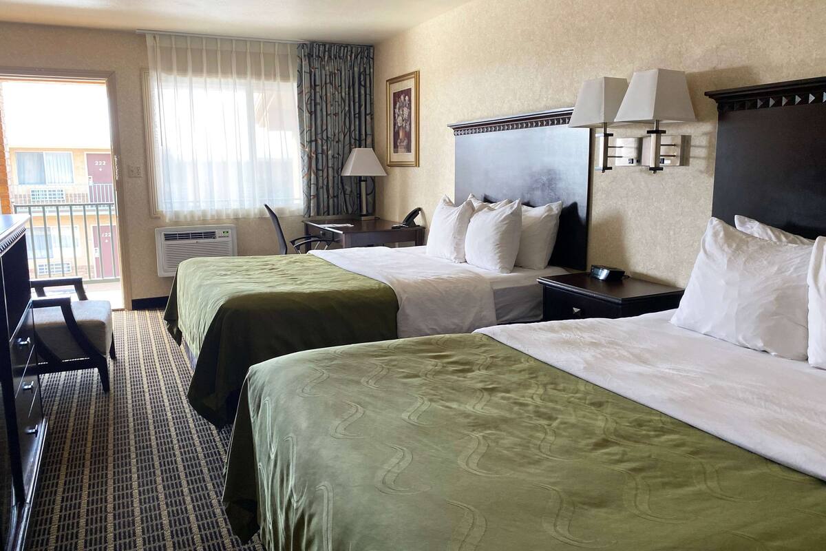Habitación de hotel con dos camas, un escritorio, una silla, una lámpara y una ventana con cortinas.