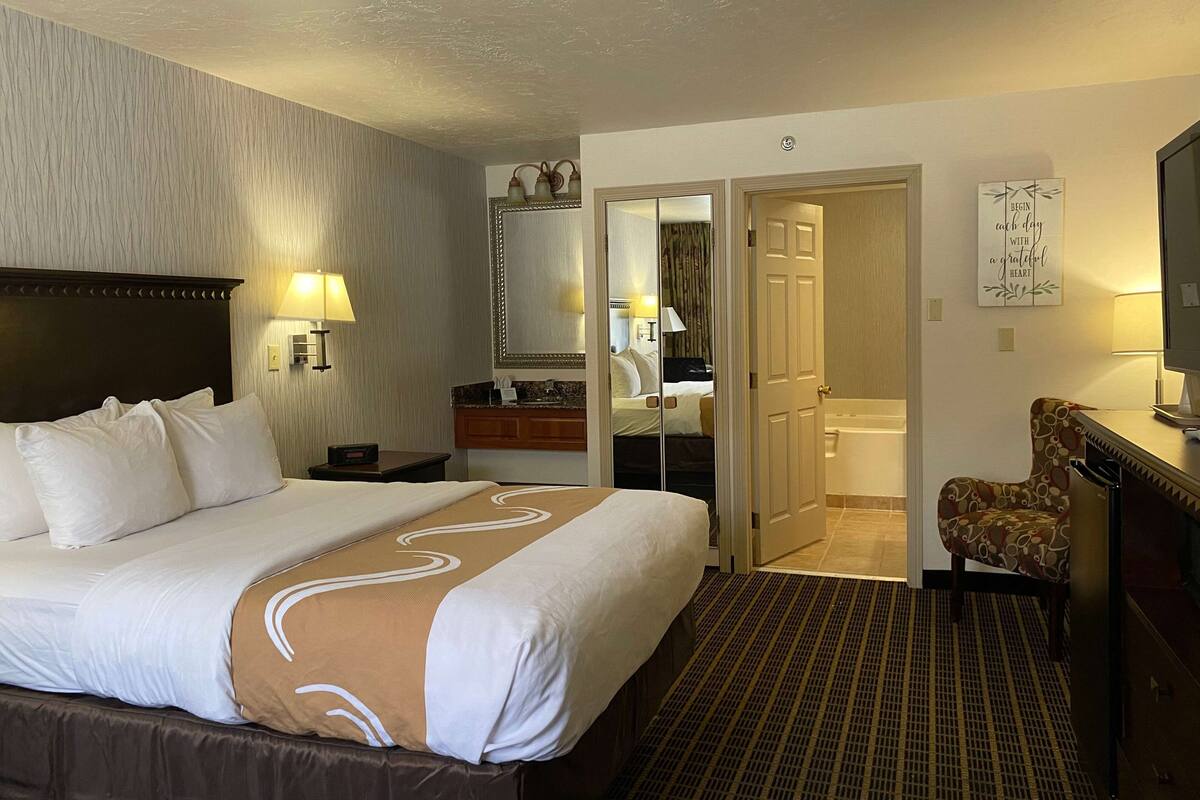 Una habitación de hotel con una cama grande, un baño, un espejo, una silla y un escritorio.