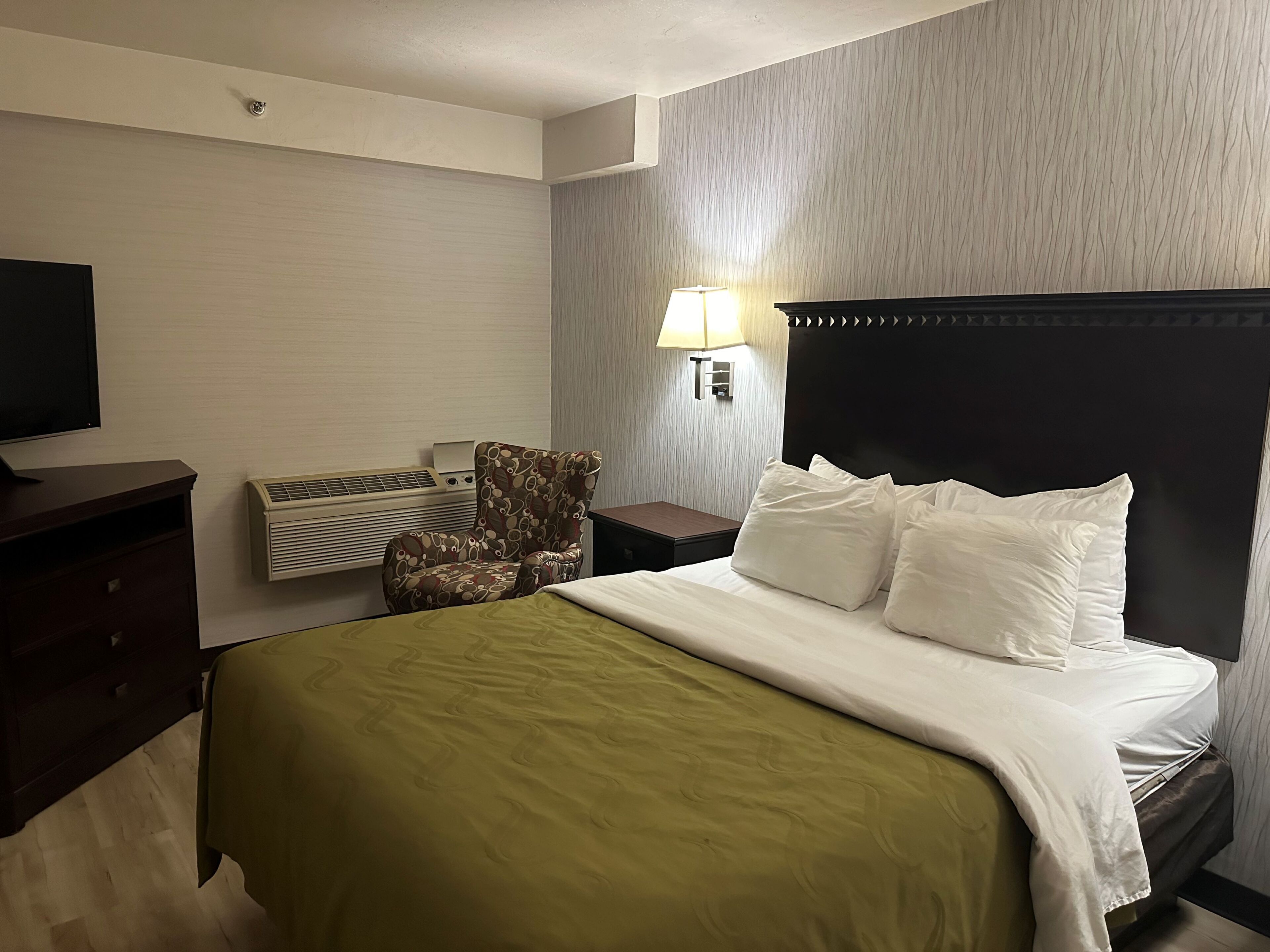 Ein Hotelzimmer mit Bett, Sessel, Fernseher, Klimaanlage und Lampe.