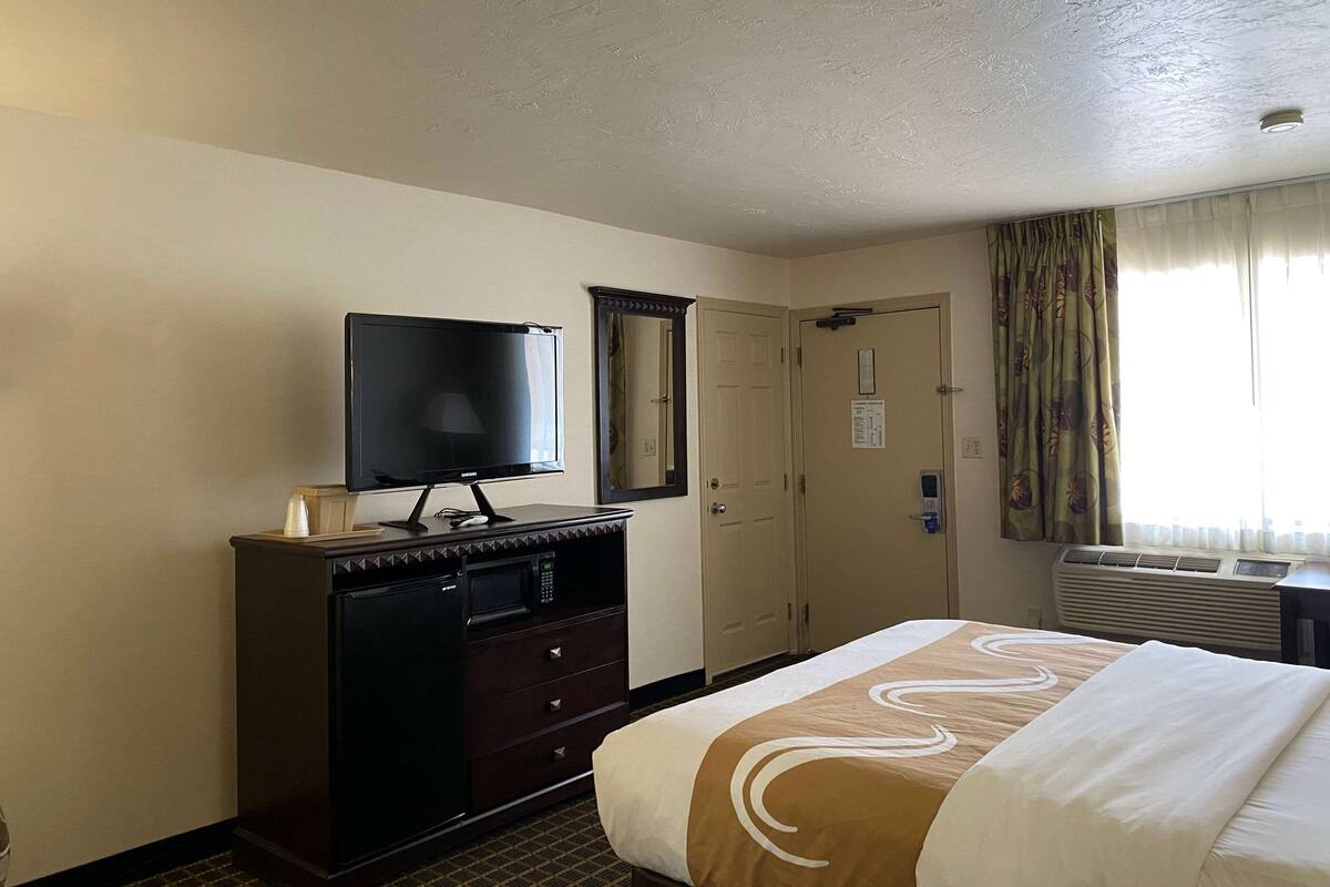 Habitación de hotel con cama, televisor en una cómoda, puerta y equipo de aire acondicionado.