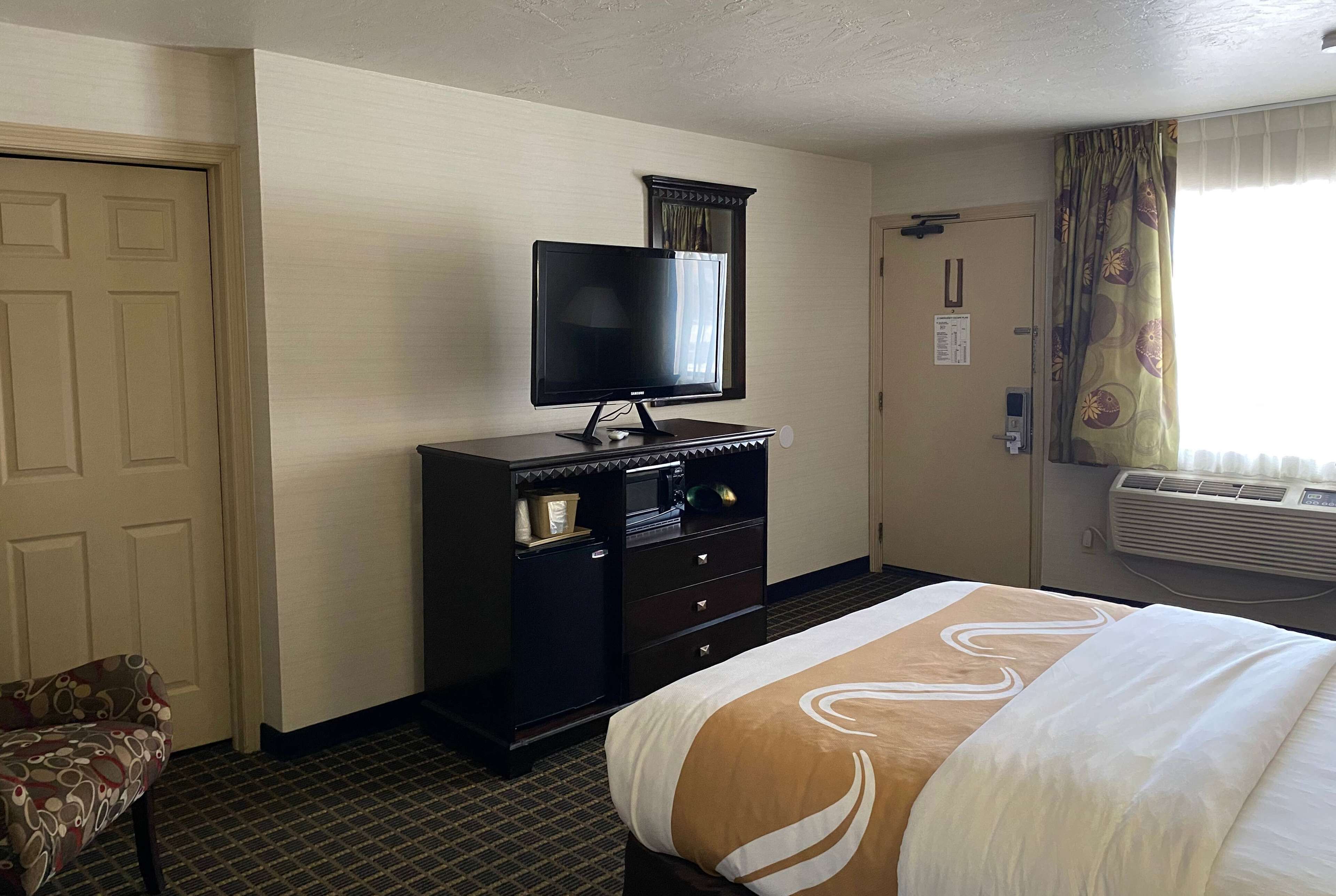 A hotel room with a bed, a TV on a dresser, a door, and an air conditioning unit.