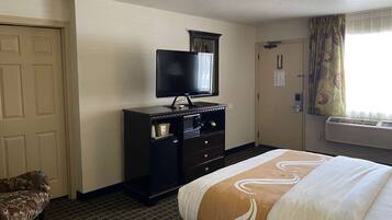 A hotel room with a bed, a TV on a dresser, a door, and an air conditioning unit.