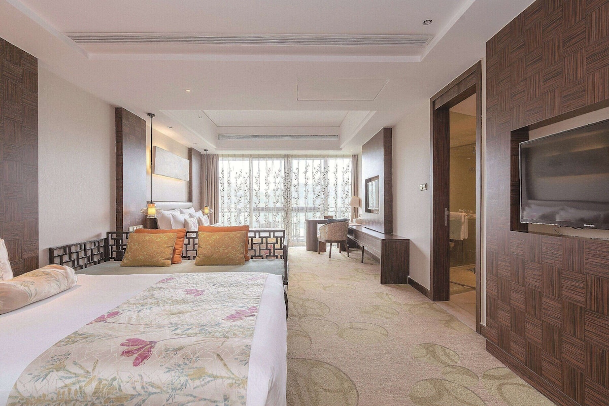 Une chambre d’hôtel avec un grand lit, un bureau, une télévision et une vue sur un jardin par la fenêtre.