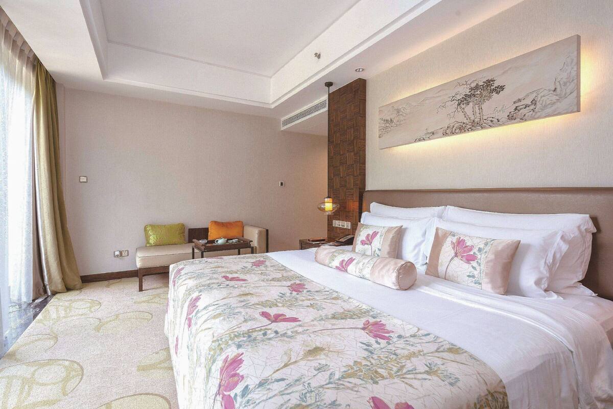 Une chambre d’hôtel avec un grand lit, une table de chevet, une chaise et une œuvre d’art accrochée au mur.