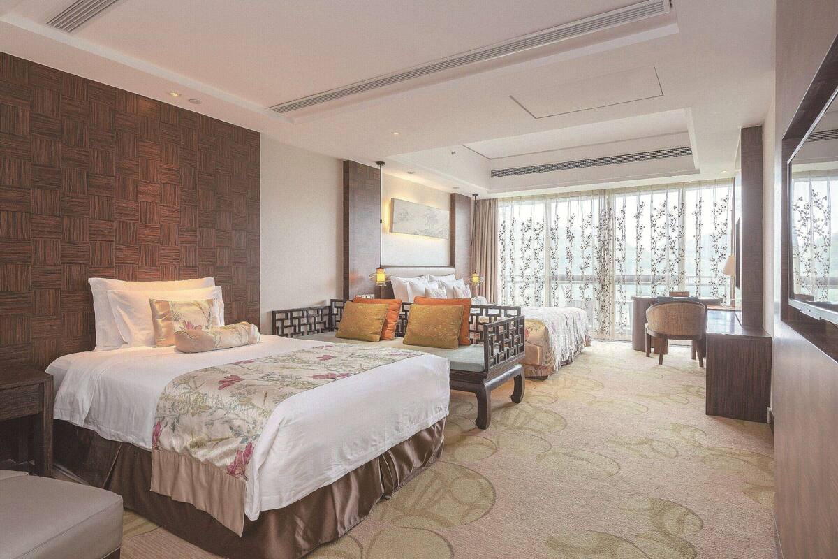 Une chambre d’hôtel avec un grand lit, un bureau et une chaise. Il y a une fenêtre avec des rideaux et une vue sur l’extérieur.