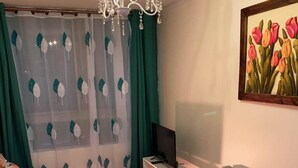 A living room with a sofa, a TV, a radiator, and a painting of tulips.